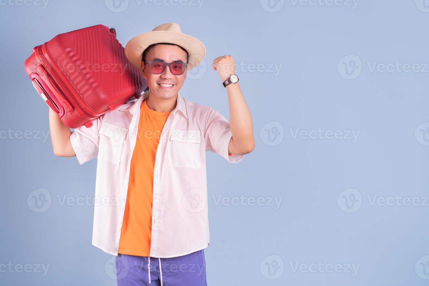 giovane uomo asiatico che tiene la valigia rossa su sfondo blu foto