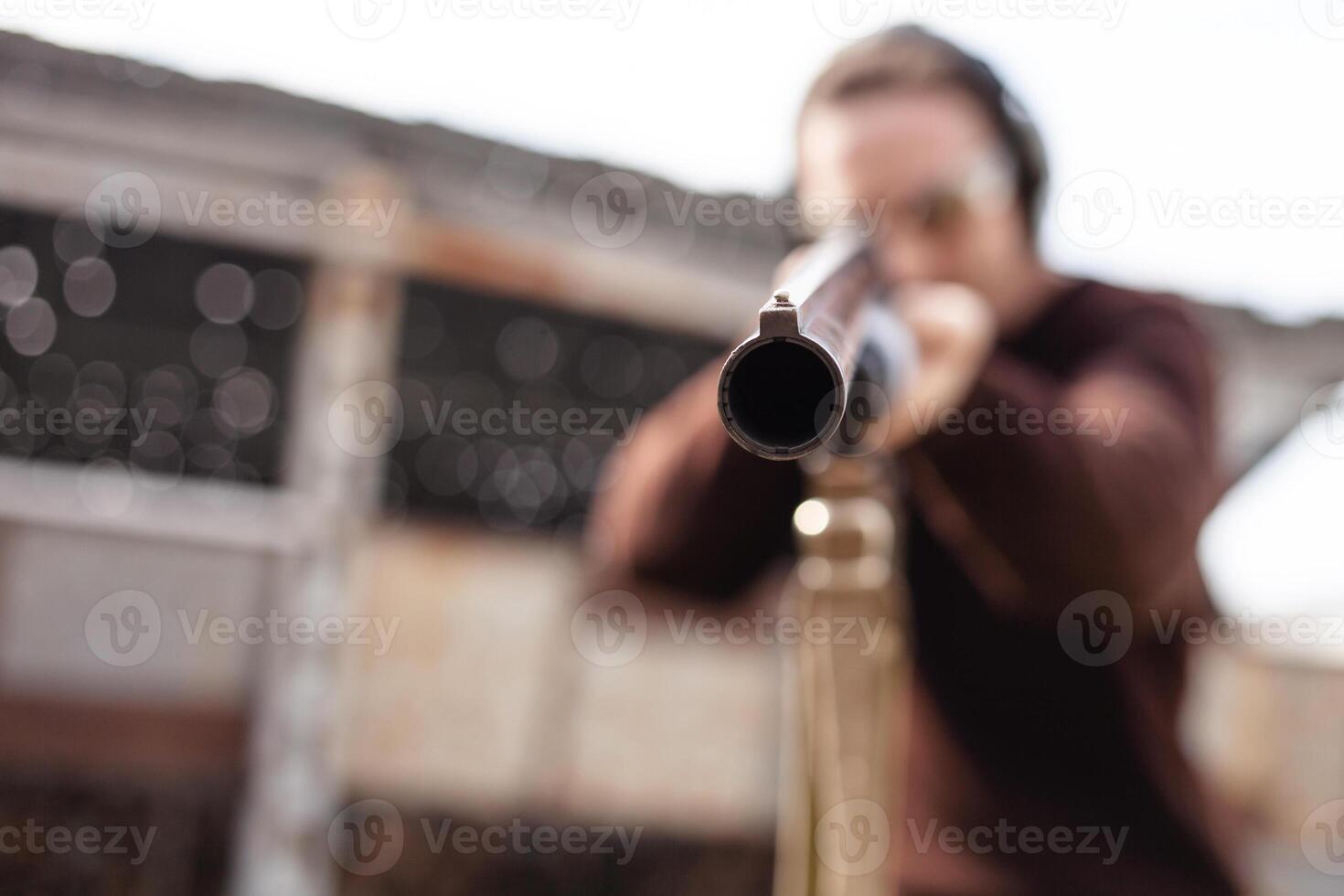 un' uomo nel protettivo bicchieri e cuffia. un' azione della pompa fucile. pneumatici all'aperto. un' parete e un' tetto con proiettile buchi. sport foto