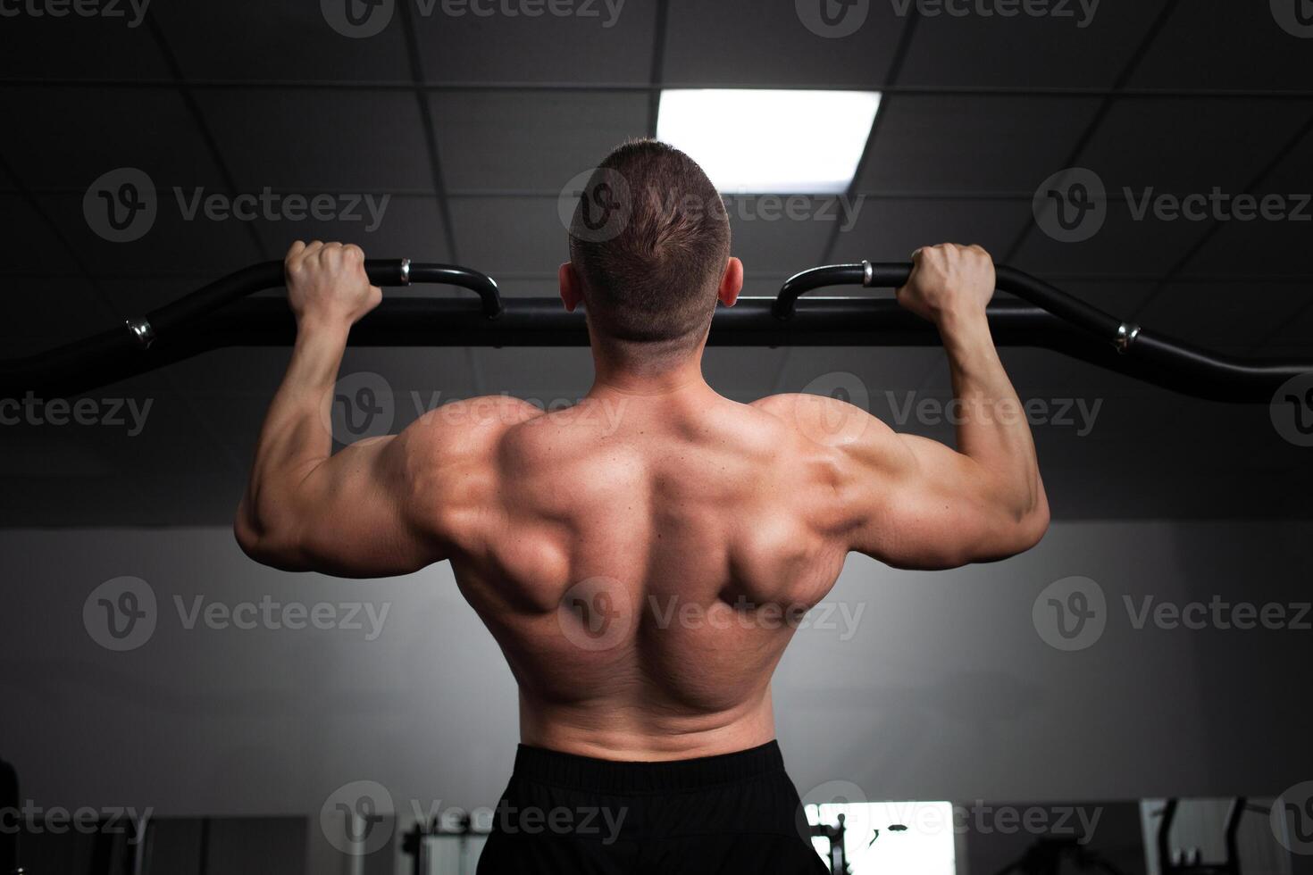 un' uomo atleta bodybuilder tira su su il suo mani, costruisce muscoli, fa un esercizio nel palestra. indietro foto