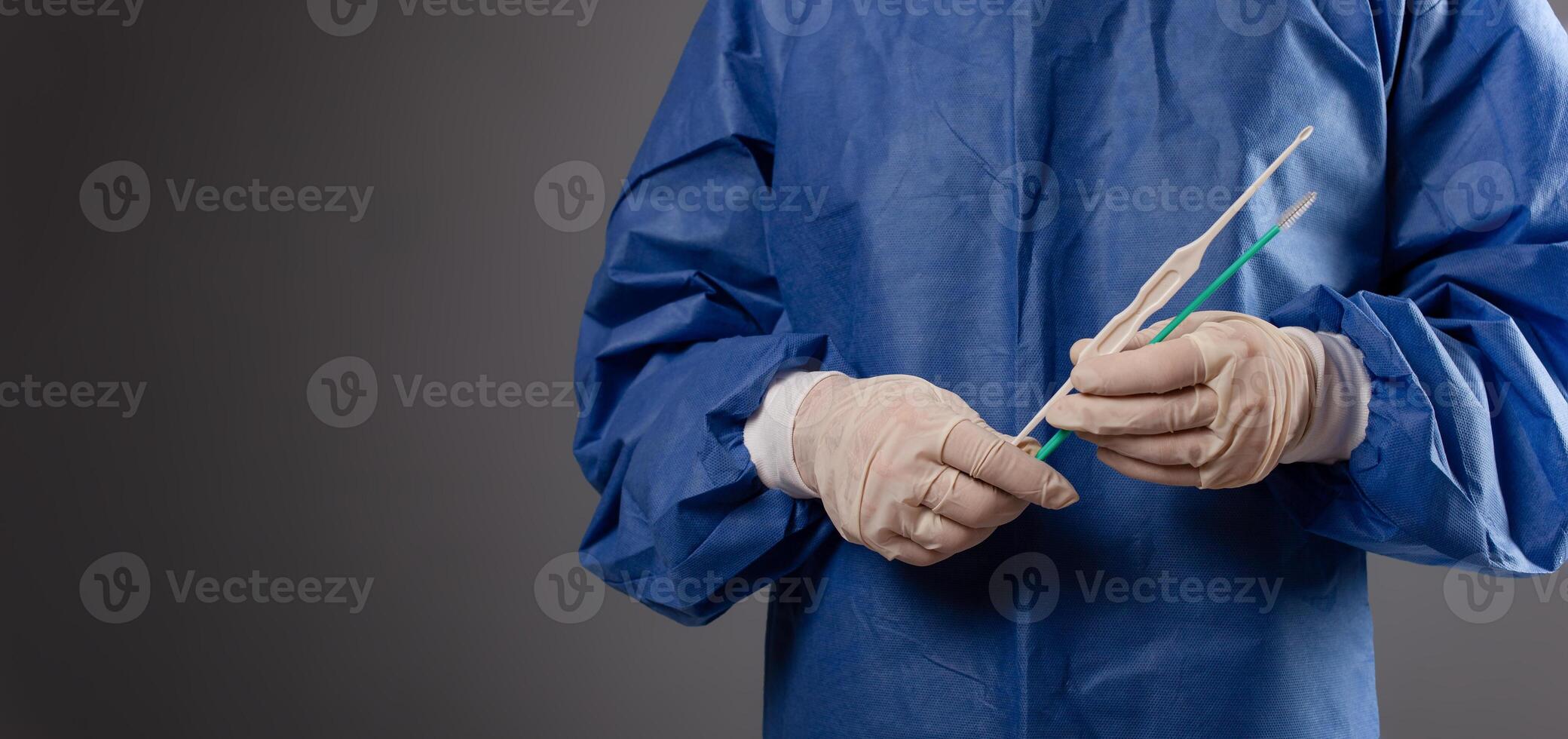 un' ginecologo con un' Venere specchio nel il suo mani. ginecologico Accessori, spazzola, bastone. un' medico nel un' medico maschera, un' veste, guanti, con un' ginecologico specchio su un' grigio sfondo. foto
