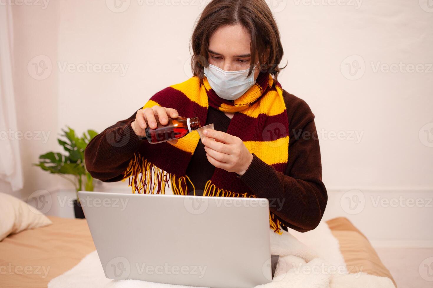 un' malato uomo si siede a un' il computer portatile indossare un' maschera. coronavirus, covid, casa quarantena. uomo versa lui stesso medicinale, ossequi influenza, raffreddori foto