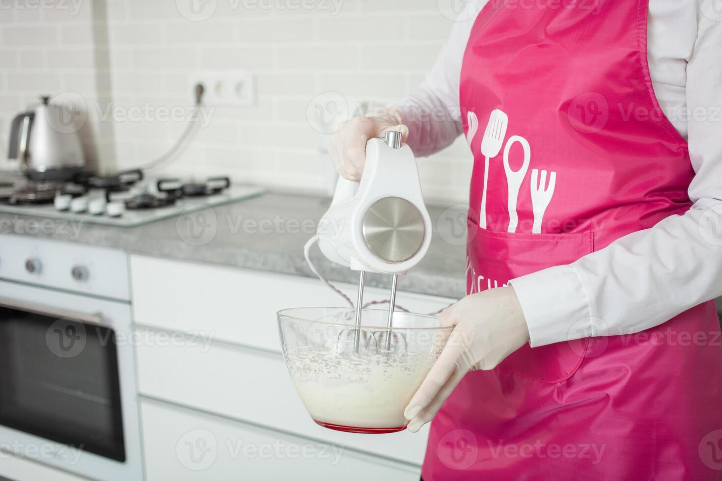 pasticciere battiti crema con mano miscelatore nel bicchiere ciotola. preparazione di dolci. bianca cucina in casa foto