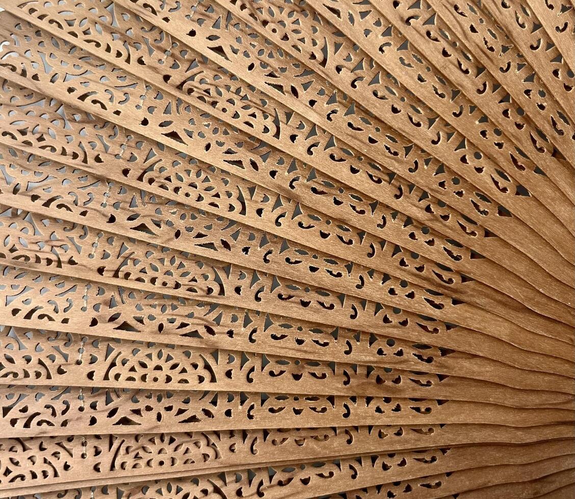 vicino su mano tenuto fan strutturato di legno sandalo Materiale e bellissimo intagli modello decorazione isolato modello. unico sfondo fotografia prospettiva. foto