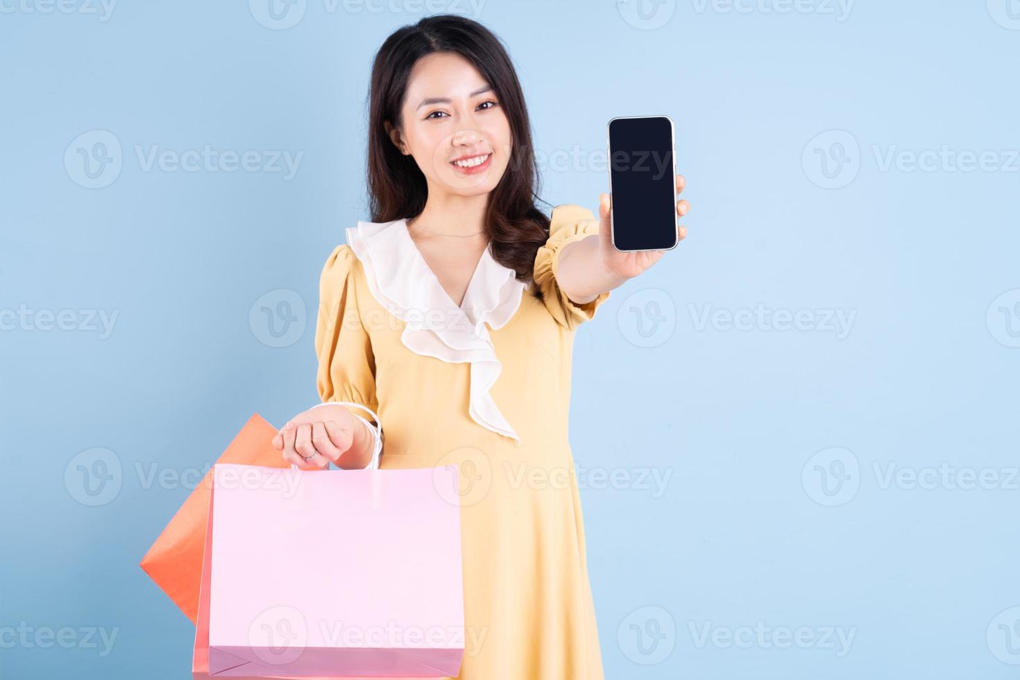 bella giovane donna asiatica che tiene la borsa della spesa su sfondo blu foto