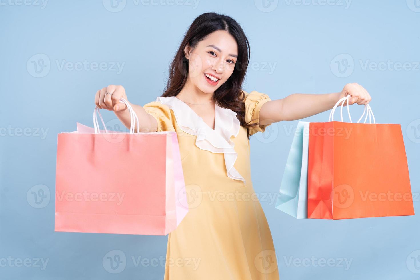 bella giovane donna asiatica che tiene la borsa della spesa su sfondo blu foto