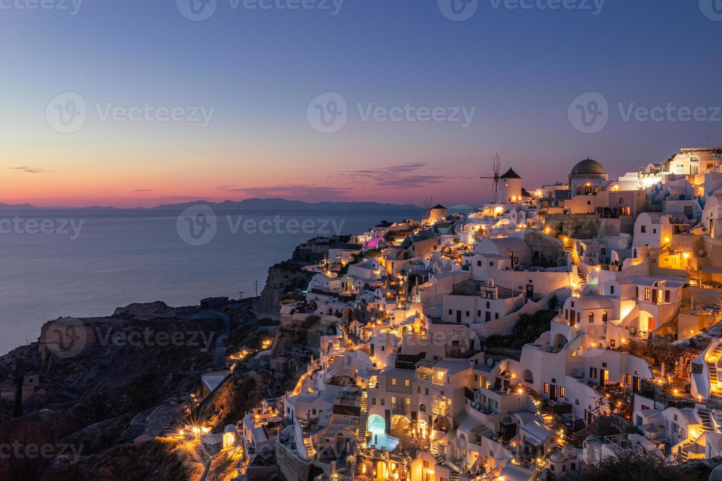 splendida isola al tramonto di santorini in grecia, bellissimo villaggio imbiancato chiesa di oia e mulino a vento durante il tramonto, luci delle strade, romantica vacanza estiva, famosa destinazione di viaggio per coppie in luna di miele foto