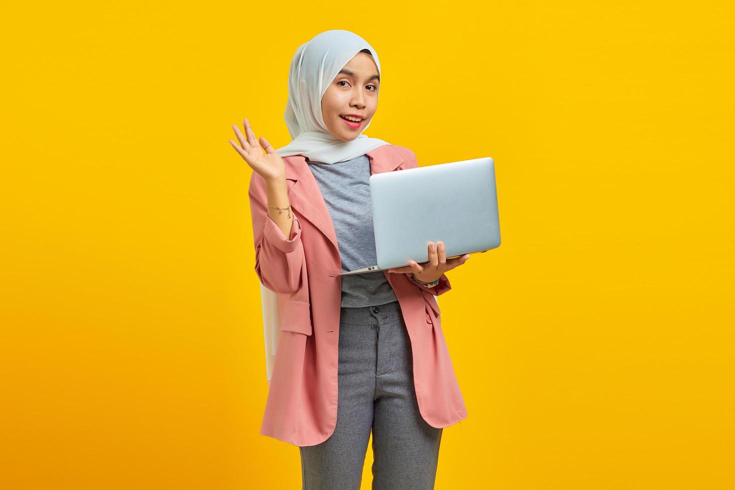 attraente giovane donna asiatica sorridente tenendo il computer portatile e saluto? foto