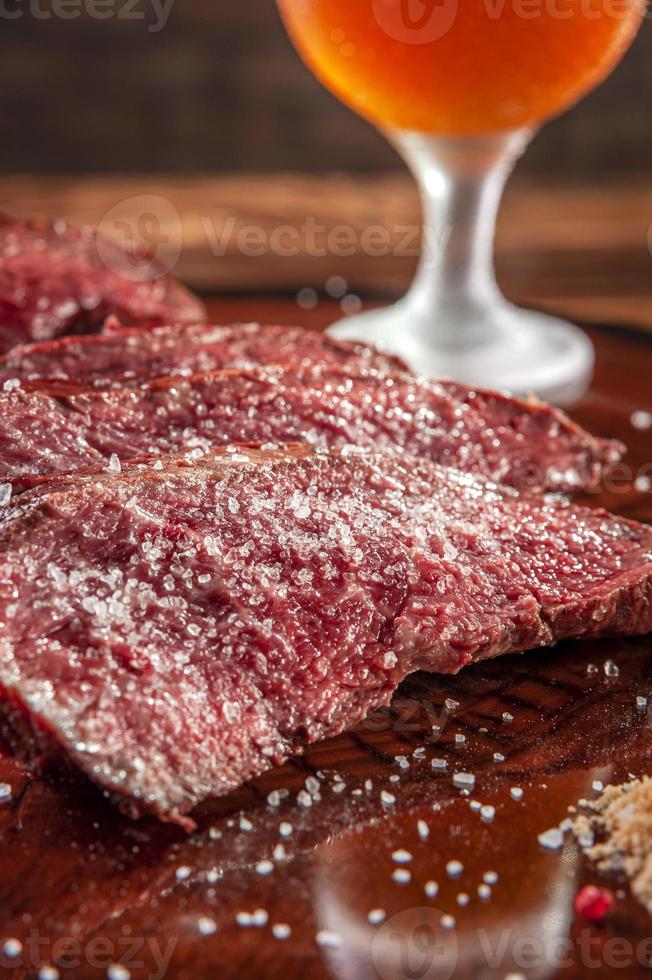 bistecca di Denver alla griglia affettata su tagliere di legno con sale parrilla e bicchiere di birra. manzo di carne di marmo - primo piano. foto