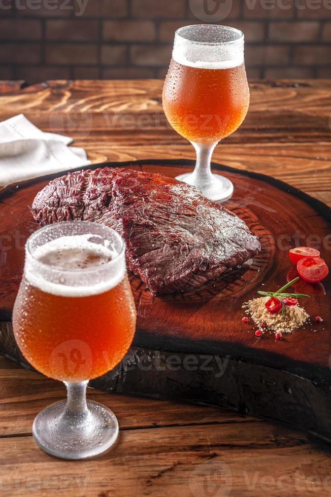 bistecca di Denver alla griglia su tagliere di legno con due bicchieri di tulipa fredda e sudati di birra alla spina. carne di manzo di marmo. foto