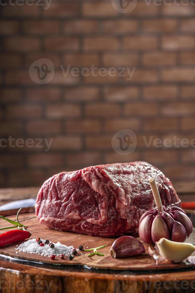 manzo crudo entrecote su un tagliere di legno con spezie su sfondo muro di mattoni - primo piano. foto