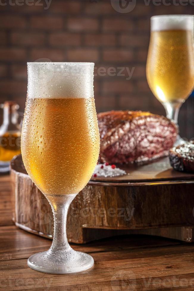 sudato freddo tulipa bicchiere di birra con bistecca di fesa di tappo affettato alla griglia su tagliere di legno - picanha brasiliana. foto