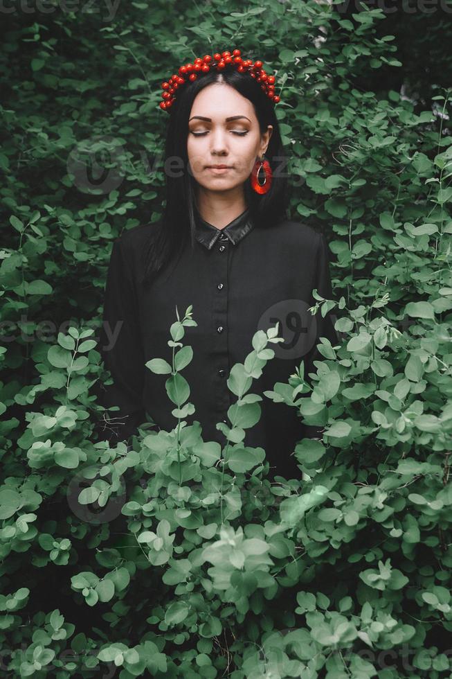 bella ragazza con gli occhi chiusi in abiti neri e orecchini rossi sullo sfondo della foresta foto