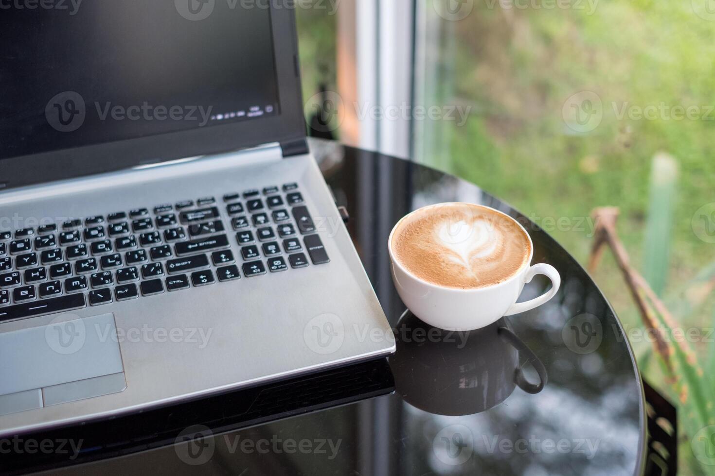 il computer portatile con latte macchiato caldo caffè nel bianca tazza su scrivania foto