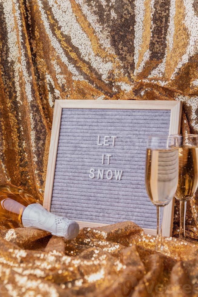 cartellone in feltro lascia che nevichi su sfondo dorato lucido con bicchieri di champagne e bottiglia foto