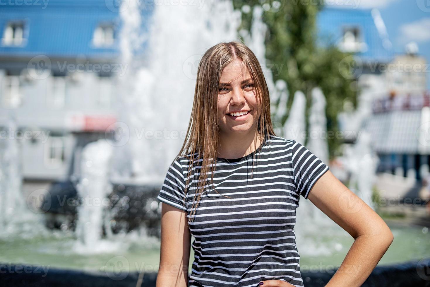 sorridenti giovane donna caucasica in abiti casual fuori in una giornata di sole vicino alla fontana foto