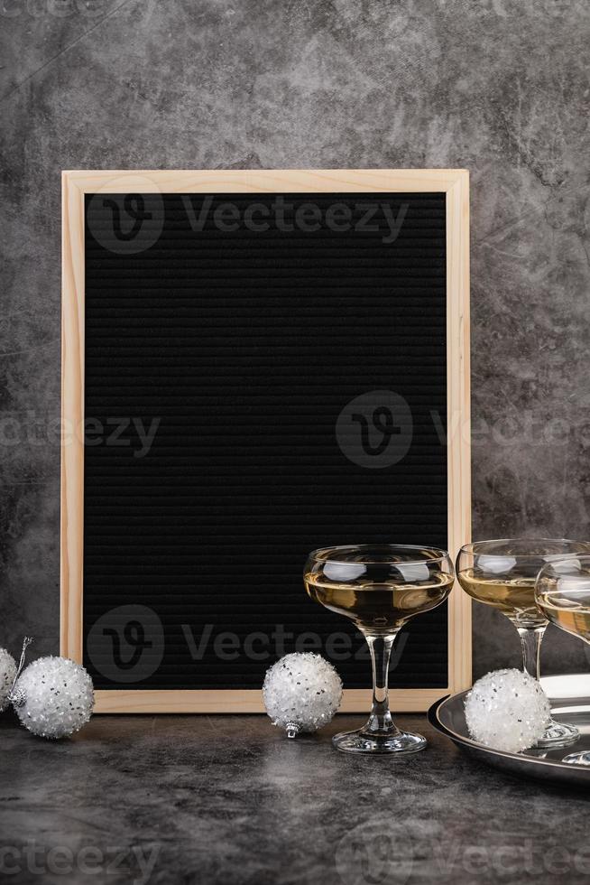 lavagna vuota in feltro nero con bicchieri di champagne e decorazioni di capodanno foto