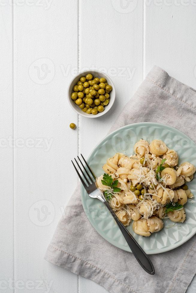 Radiatori di pasta con besciamella con piselli, formaggio e prezzemolo in piatto colorato alla menta su fondo di legno foto