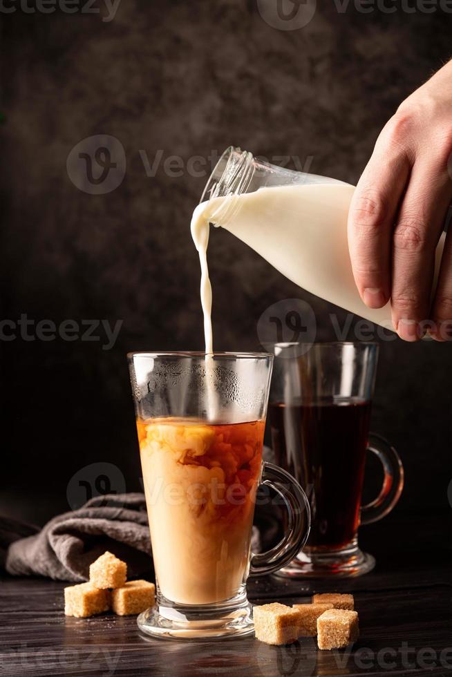 mano maschio versando il latte nella vista frontale del tè nero caldo su sfondo scuro foto