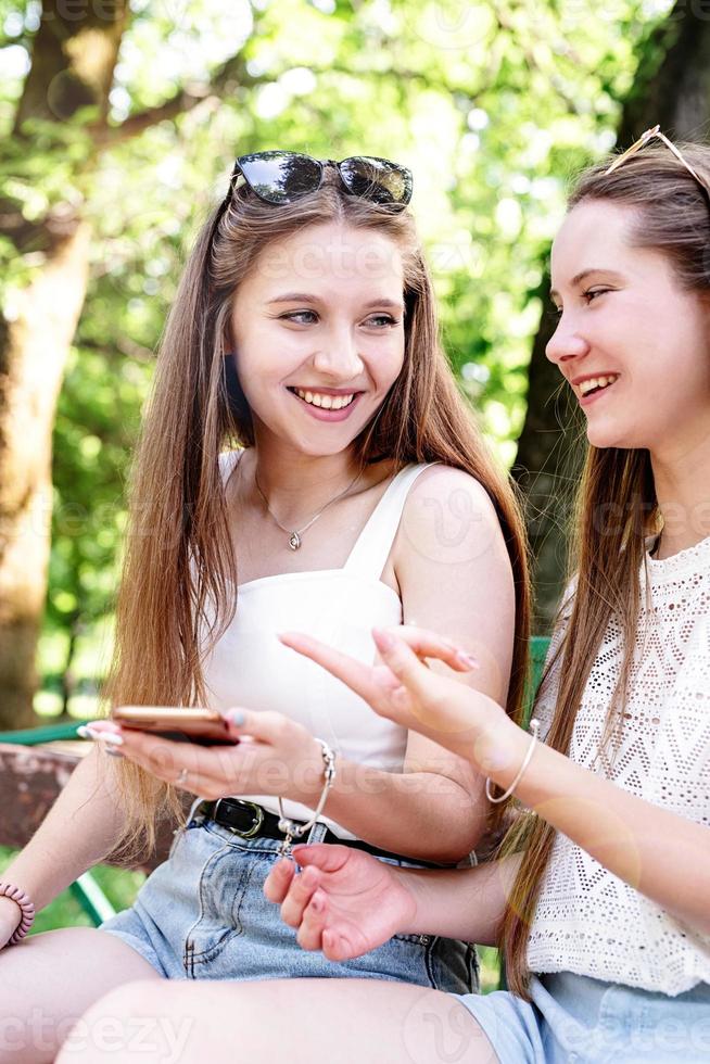 due donne felici che parlano nel parco usando il cellulare foto