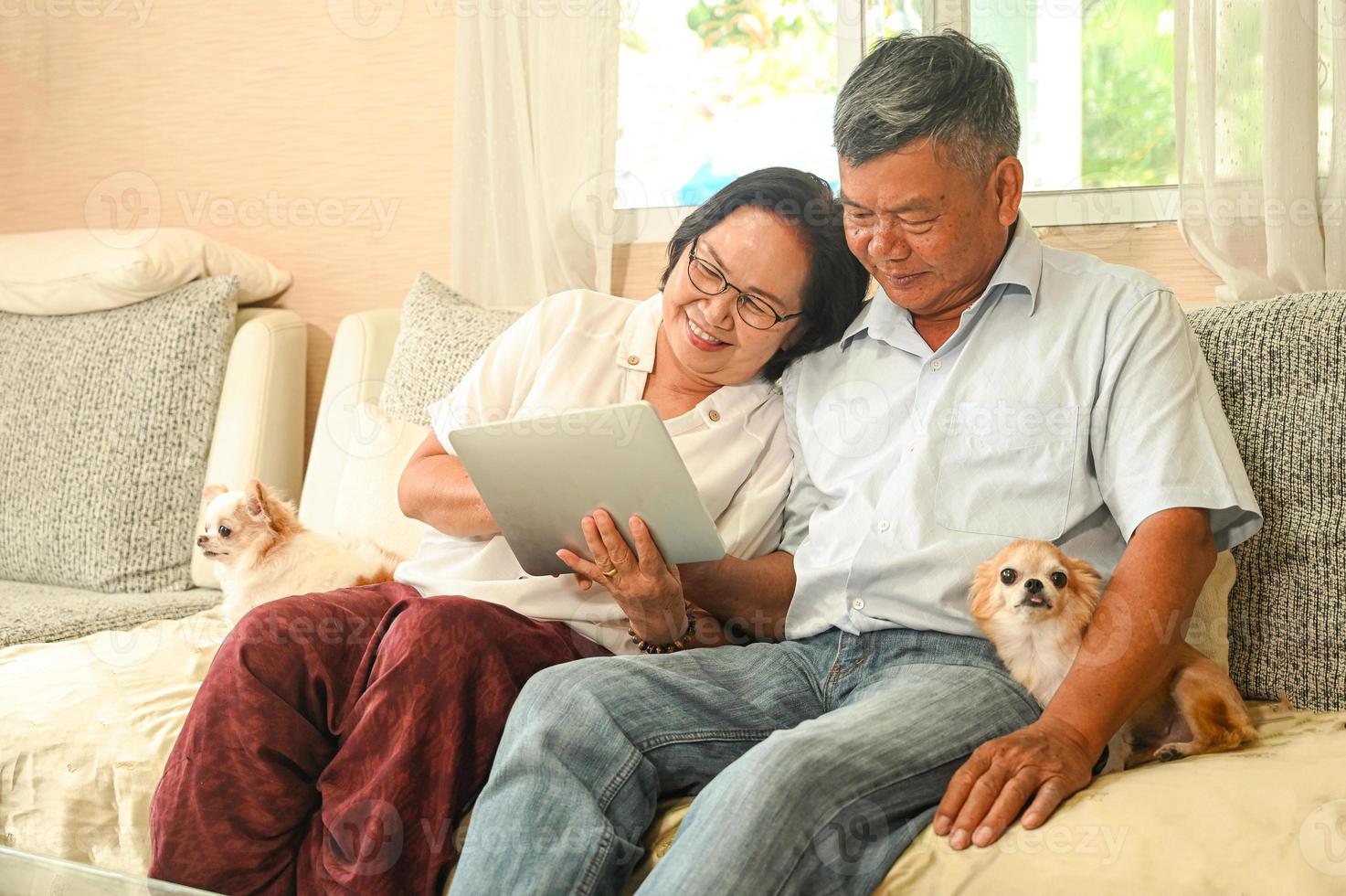 una donna anziana e un uomo asiatico seduti su un divano stanno usando un tablet. foto