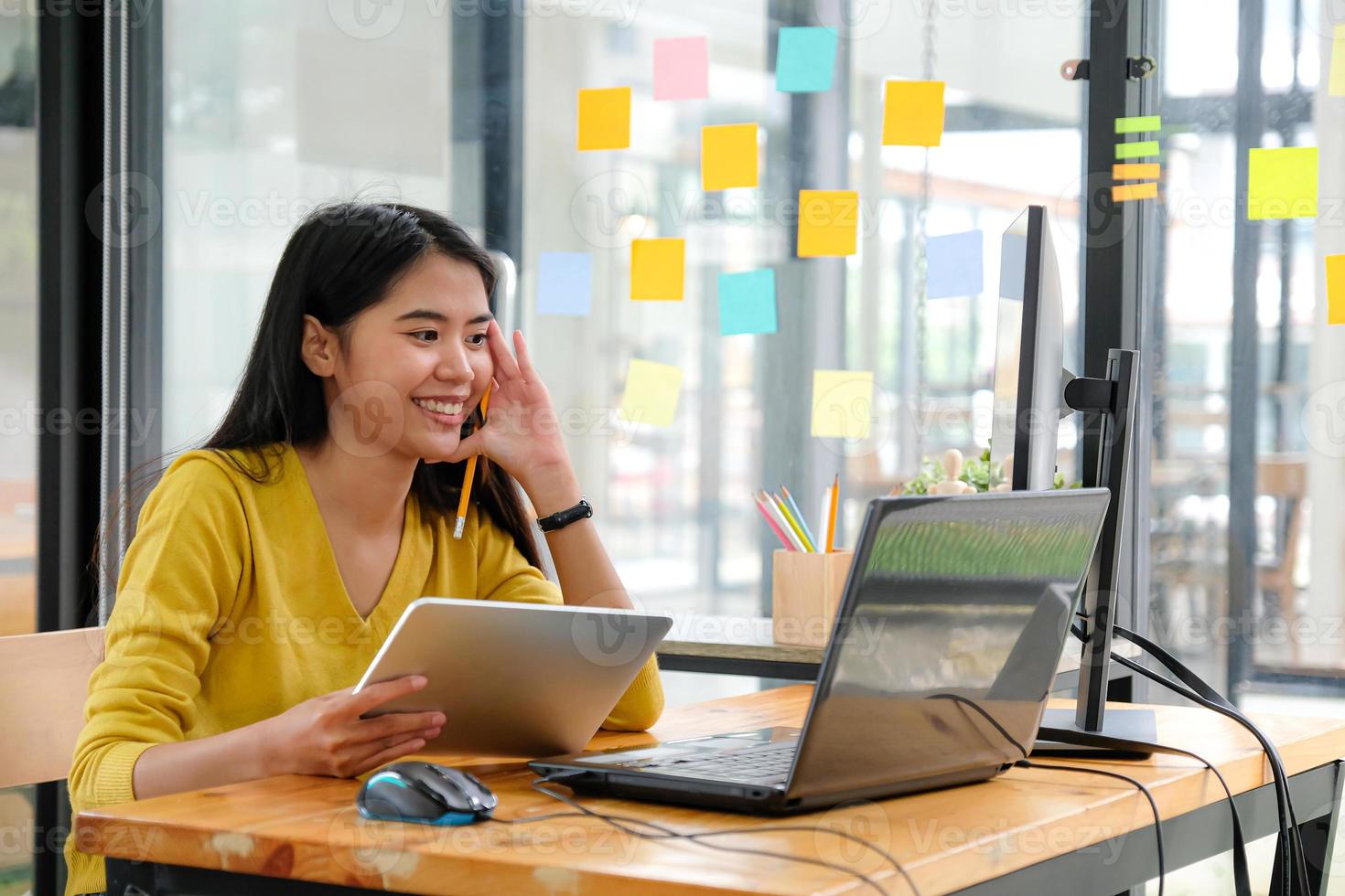 programmatrice asiatica, che indossa una maglietta gialla, guarda lo schermo del laptop, tiene in mano un tablet e una matita. sembrava felice. foto