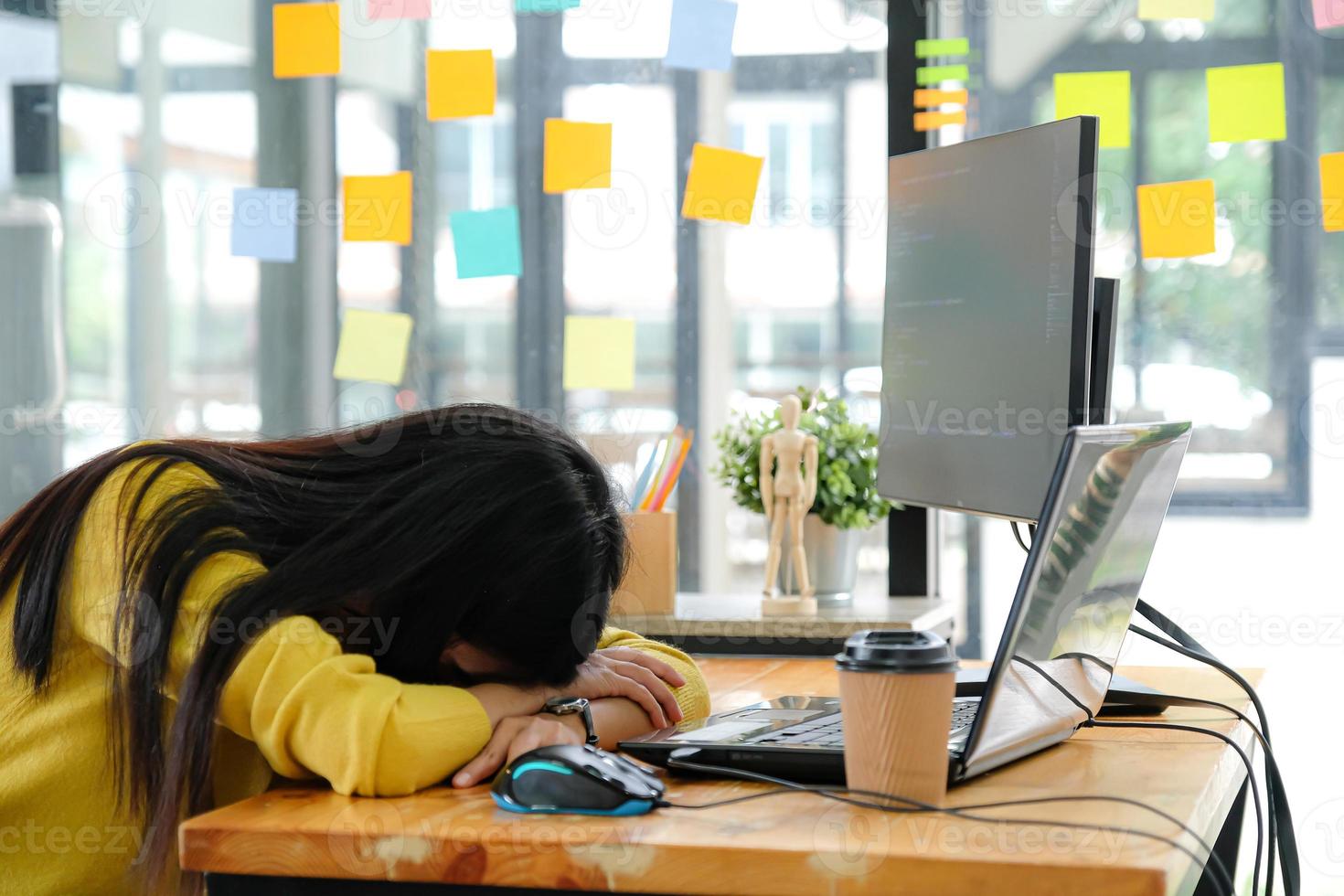 programmatore femminile asiatico che indossa una camicia gialla e si inchinò sulla sua scrivania in ufficio. foto