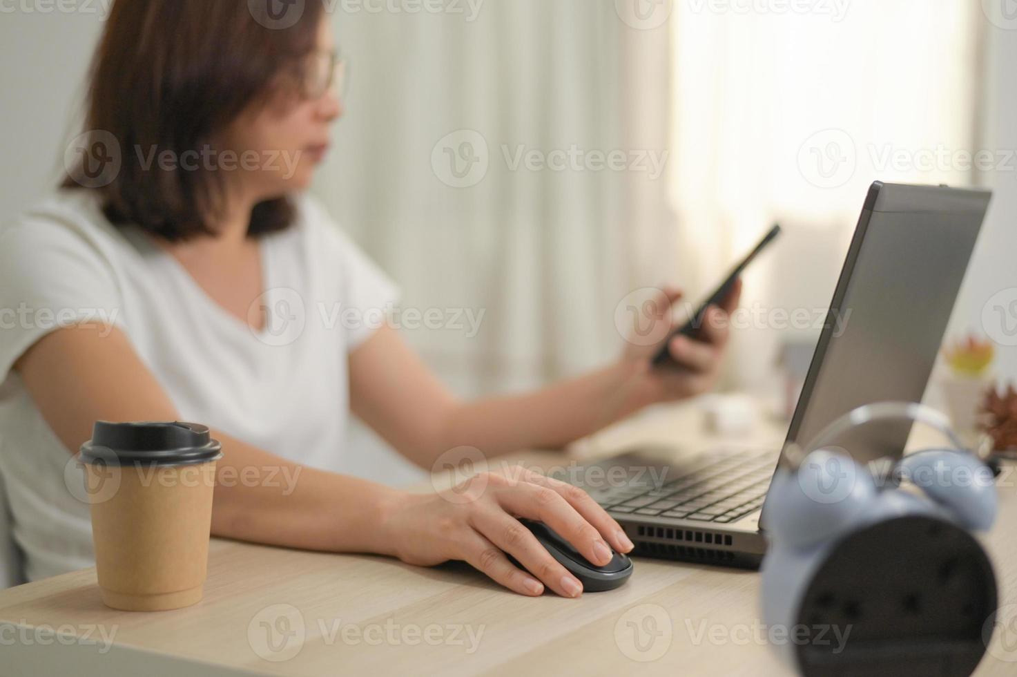 una mano di una donna che tiene su un mouse usando un laptop che lavora da casa. foto