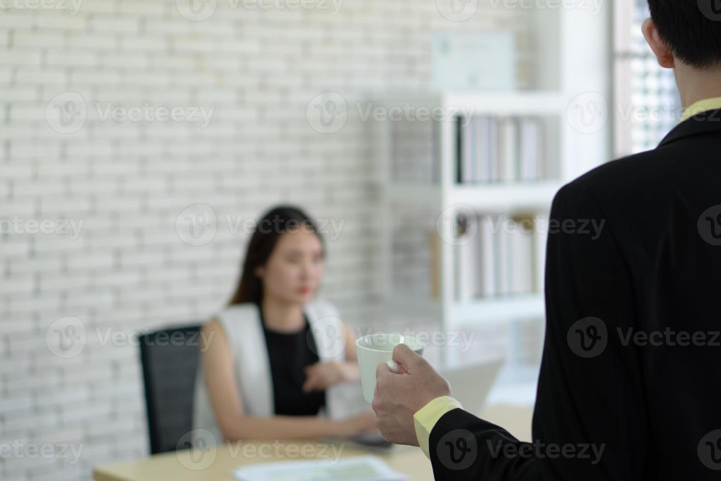 uomo in tuta che porge il caffè a una giovane donna d'affari asiatica che lavora in ufficio foto