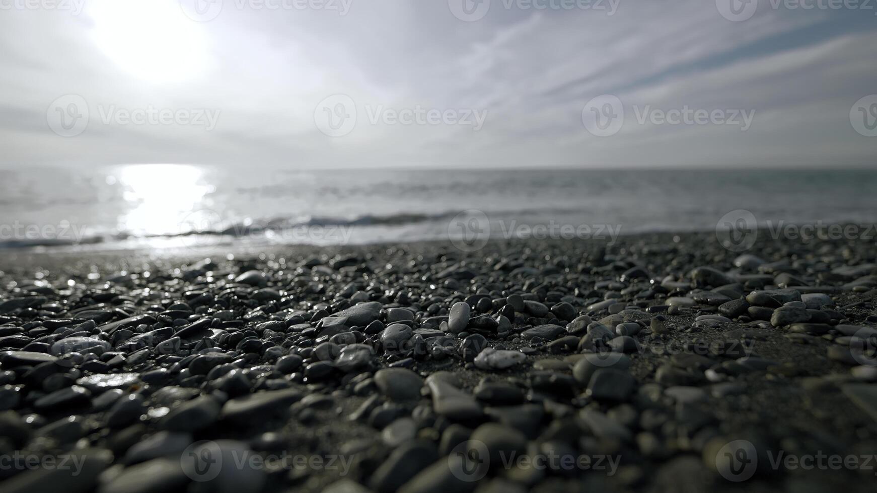 bellissimo abbandonato spiaggia. azione.luminoso onde di il mare battito su piccolo pietre e voi può vedere il luminosa sole splendente direttamente in il telecamera. foto