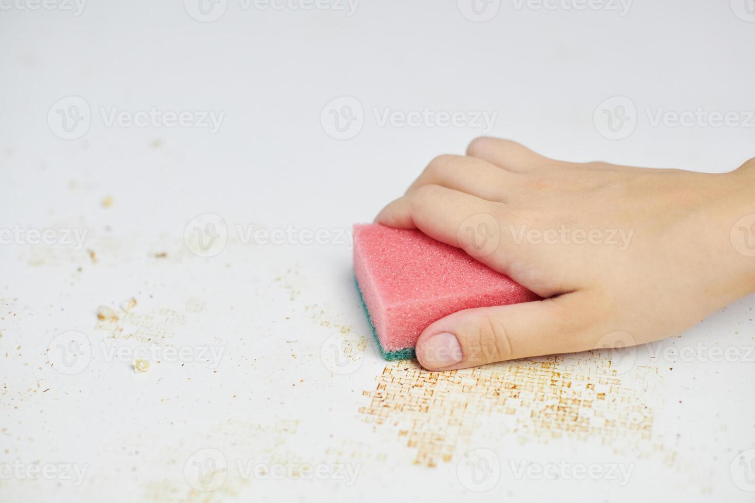 pulire il tavolo della cucina. la spugna rosa in mano della donna rimuove lo sporco, il pangrattato e gli avanzi. faccende domestiche foto