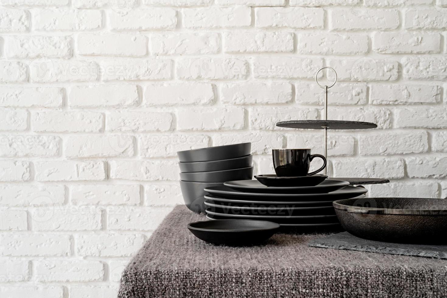 pila di piatti in ceramica nera e stoviglie sul tavolo su sfondo bianco muro di mattoni foto
