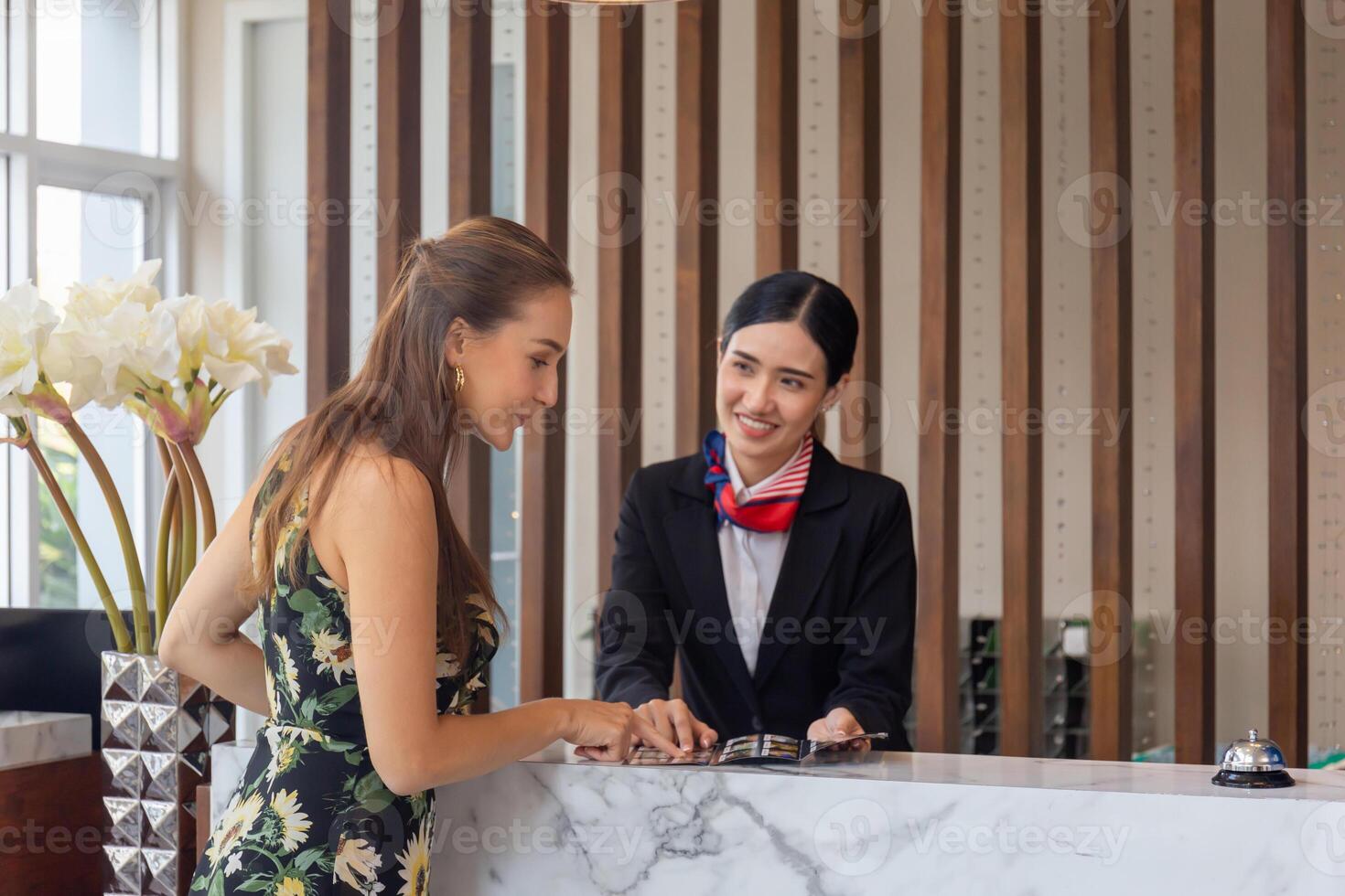 messa a fuoco su femmina i viaggiatori con Borsa viaggio bagaglio registrare a il Hotel con sfocato sorridente femmina addetto alla reception foto