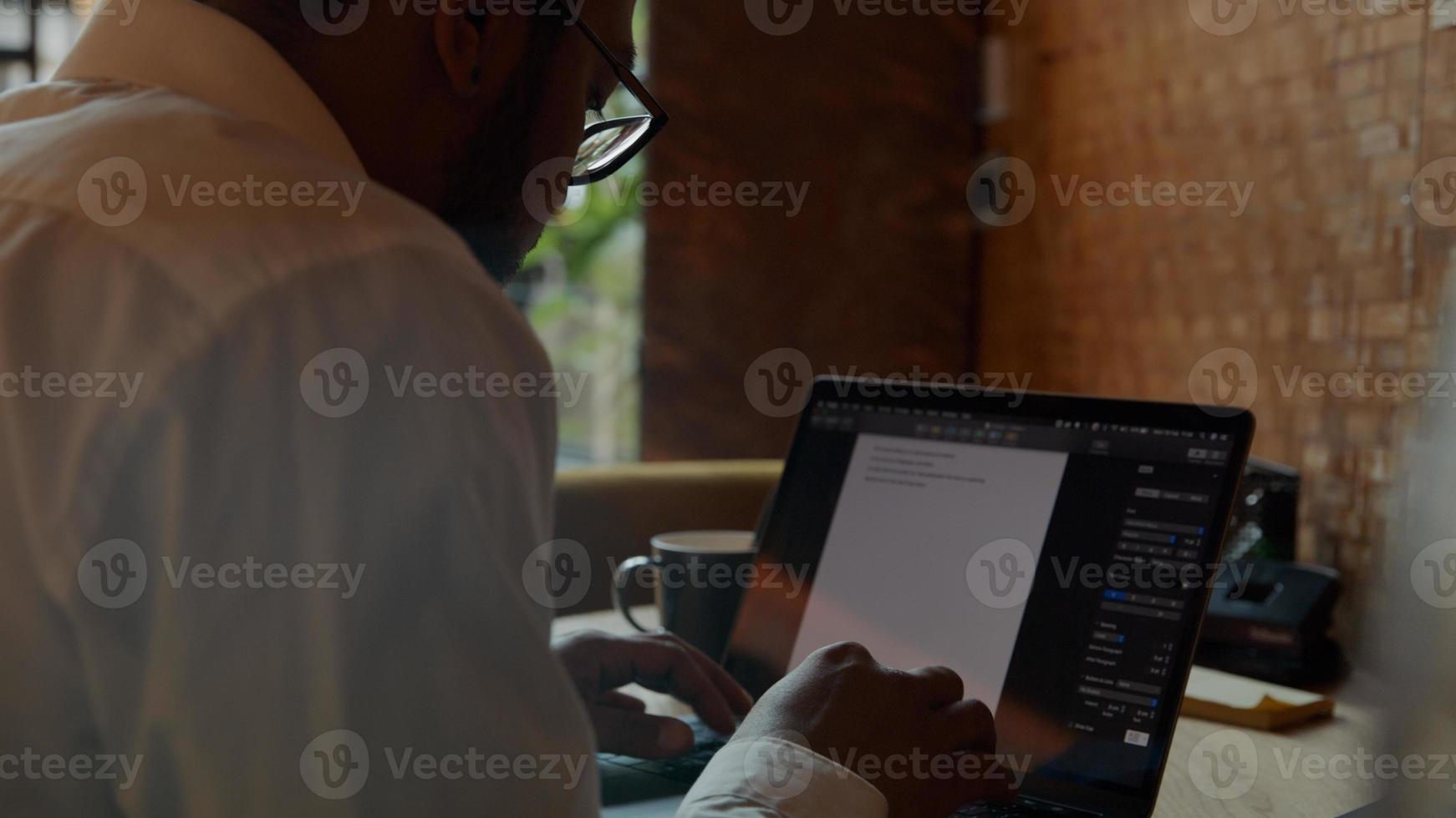 uomo nero con gli occhiali, seduto al tavolo, digitando sul laptop foto