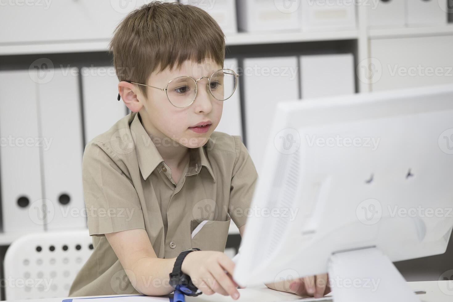 un' bambino con bicchieri a il computer. scolaro sembra a il tenere sotto controllo schermo foto