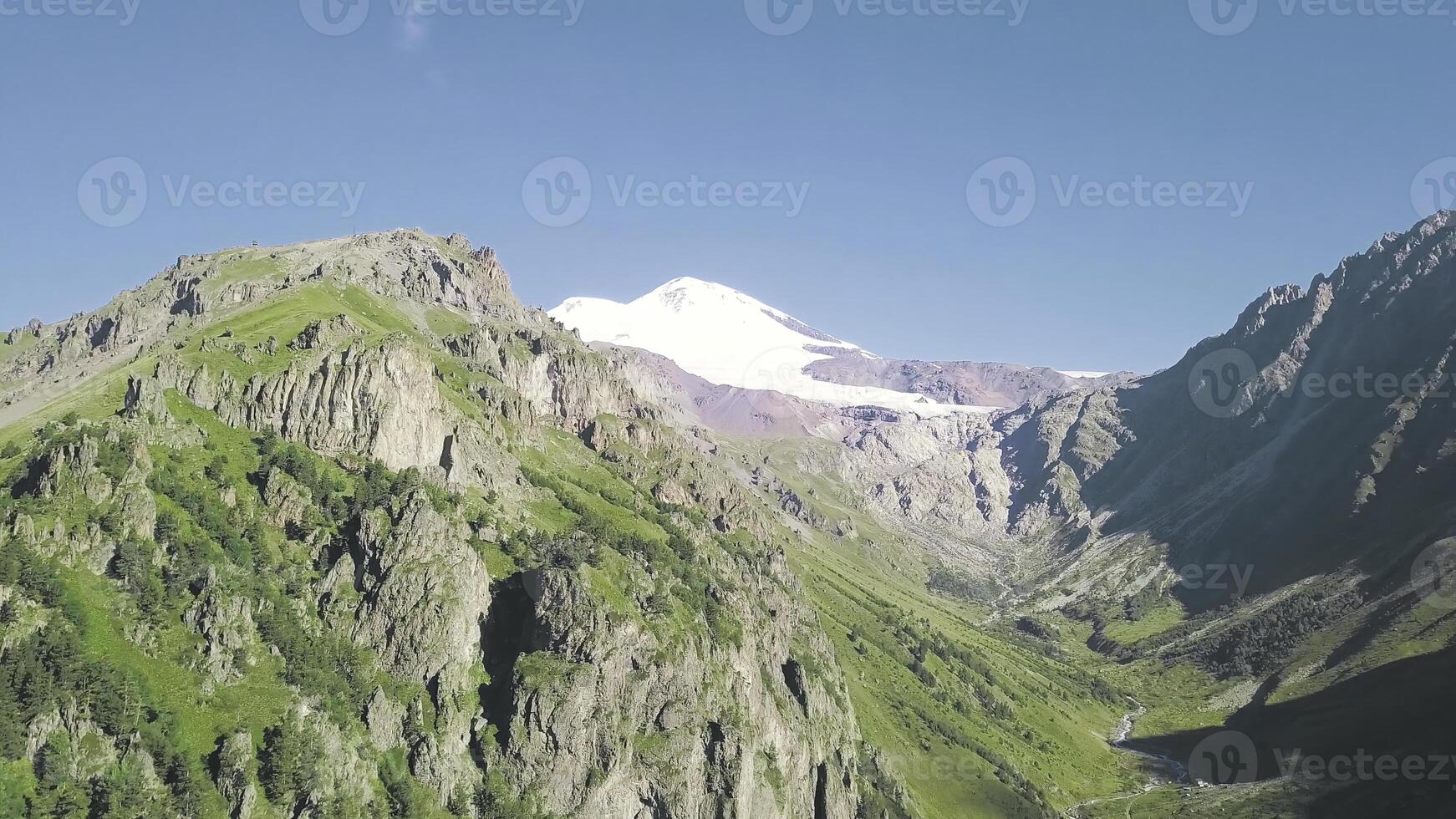 superiore Visualizza di montagna paesaggio con nevoso picco e verde piste. clip. maestoso roccioso montagne con verde foresta e snow-capped picchi. spettacolare montagna paesaggio su soleggiato giorno foto