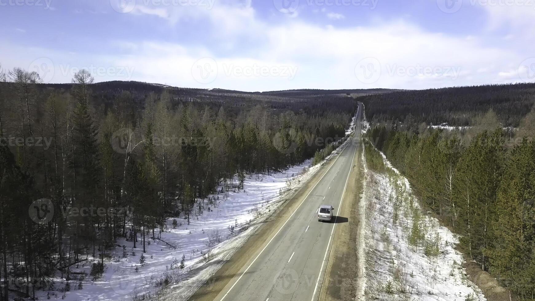 volante al di sopra di il calcestruzzo strada con in movimento veicolo lungo il pino albero foresta. clip. aereo Visualizza di neve coperto terra nel il foresta e in ritardo autunno nazione strada con un' guida macchina. foto