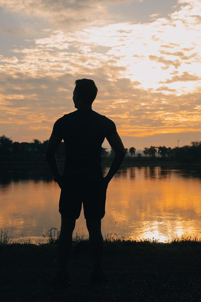 indietro Visualizza silhouette di un' corridore uomo in esecuzione su il spiaggia a tramonto con sole nel il sfondo foto