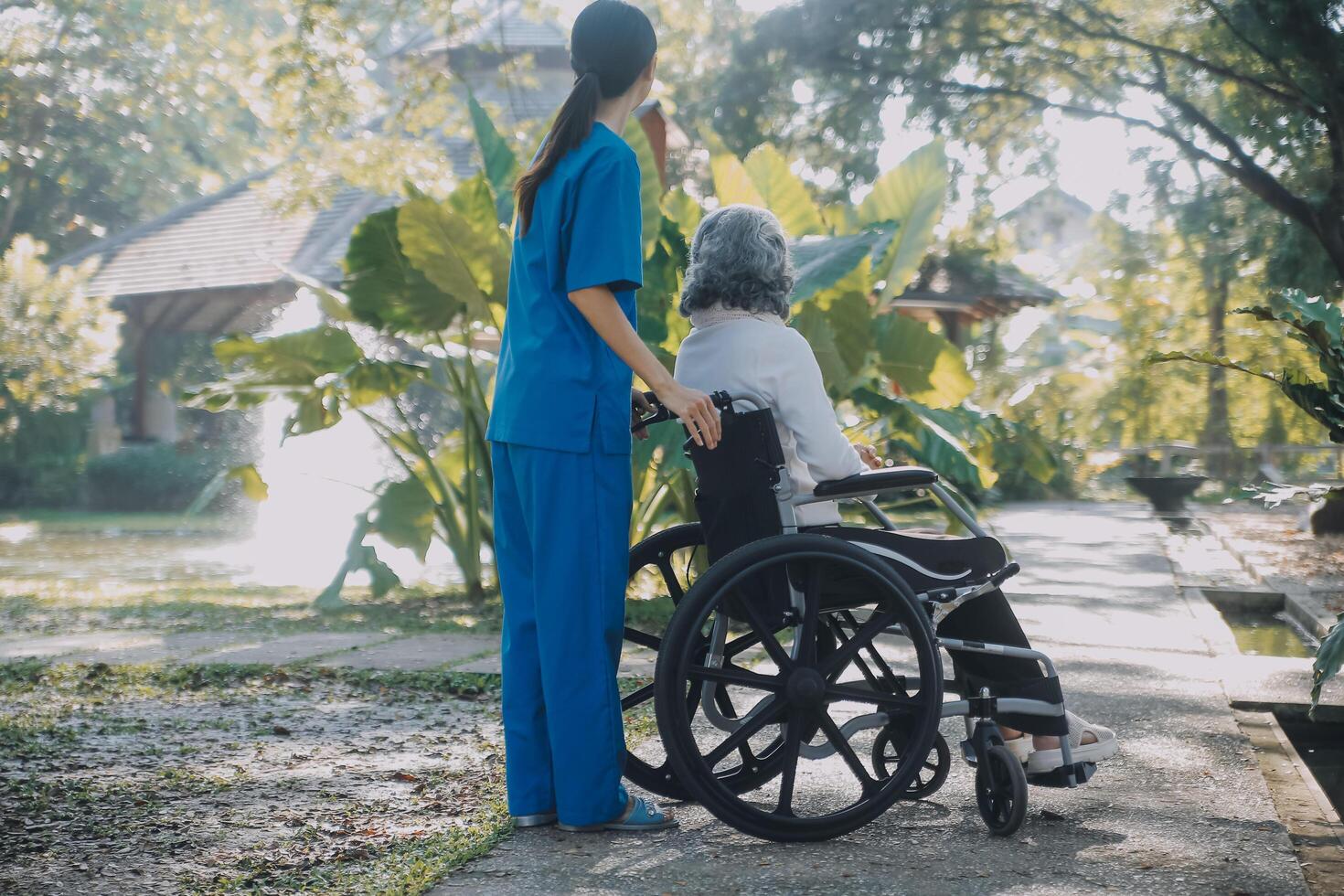 un' infermiera prendere cura un' anziano maschio su sedia a rotelle nel il suo giardino a casa foto