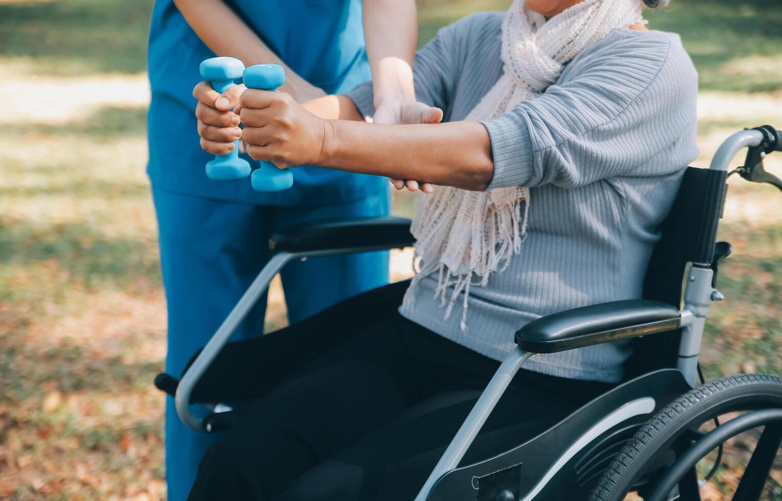 giovane infermiera o fisioterapista nel scrub porzione un' contento pensionato vecchio donna fare fitness esercizi con leggero peso manubri a casa. concetto di fisioterapia per gli anziani foto