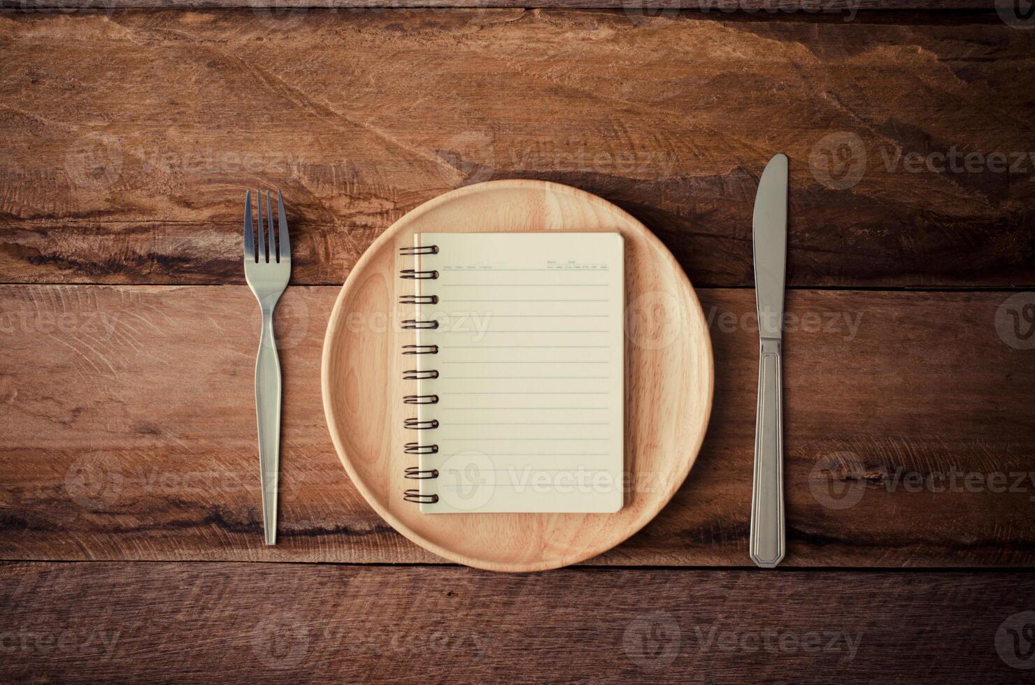 taccuino nel il di legno piatto con un' cucchiaio e un' coltello posa accanto un' tavolo, concetto per percezione foto