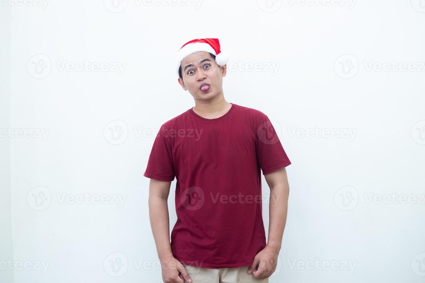 giovane asiatico uomo indossare un' Santa Claus cappello attaccare su il suo lingua e beffardo isolato di un' bianca sfondo per visivo comunicazione foto