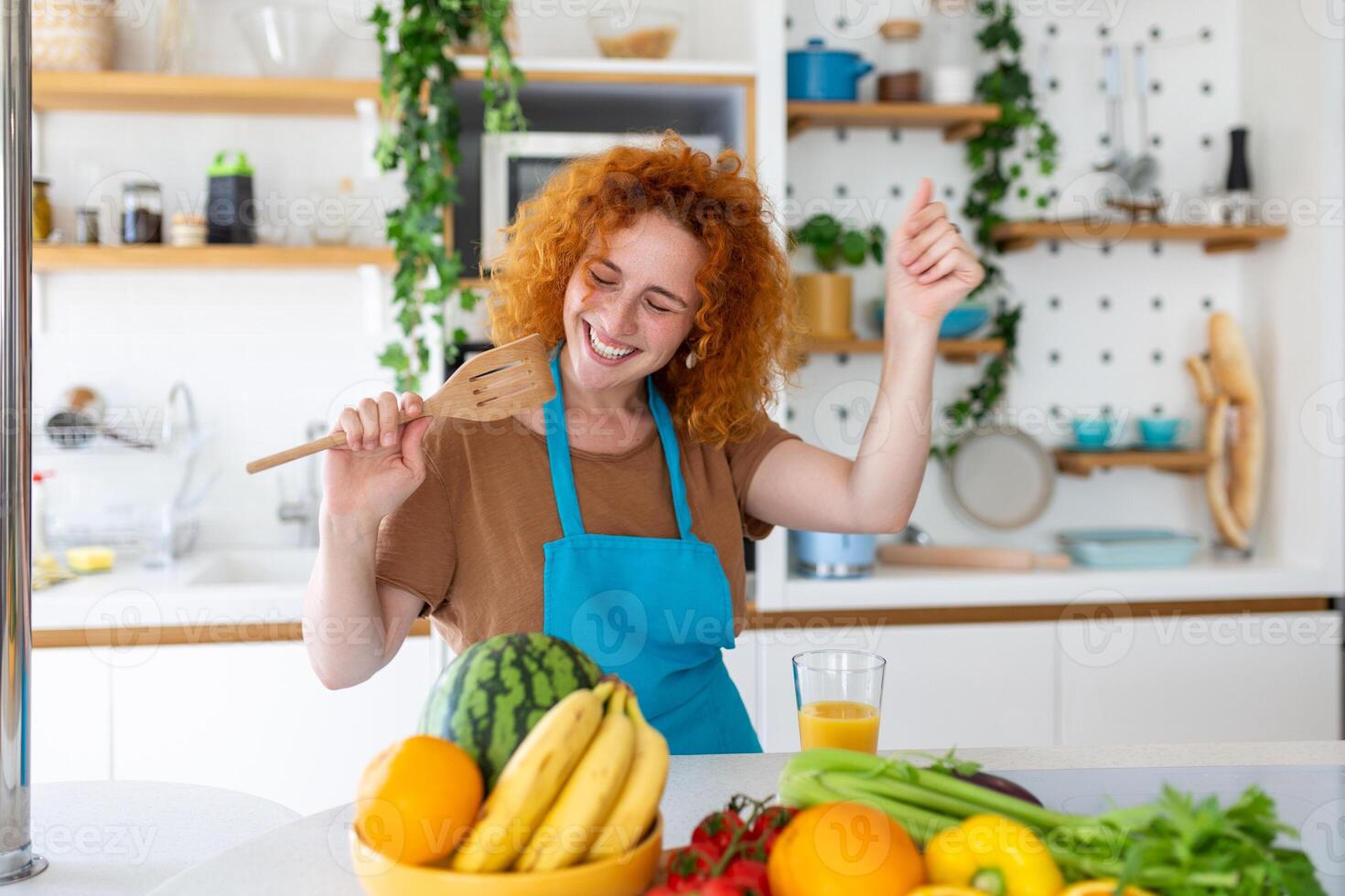 divertente bellissimo donna cantando in spatola, cucinando nel moderno cucina, Tenere spatola come microfono, ballare, ascoltando per musica, giocoso ragazza avendo divertimento con stoviglie, preparazione cibo. foto