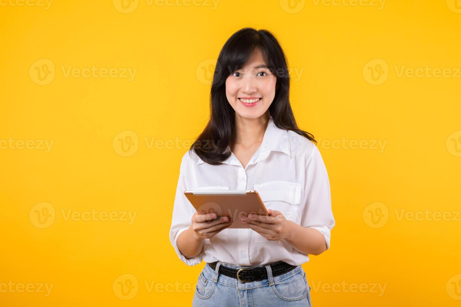 giovane asiatico donna indossare bianca camicia sorrisi brillantemente mentre Tenere digitale tavoletta contro giallo sfondo, rappresenta un' fiducioso azienda lavoratore Abbracciare una persona moderno tecnologia concetti. foto