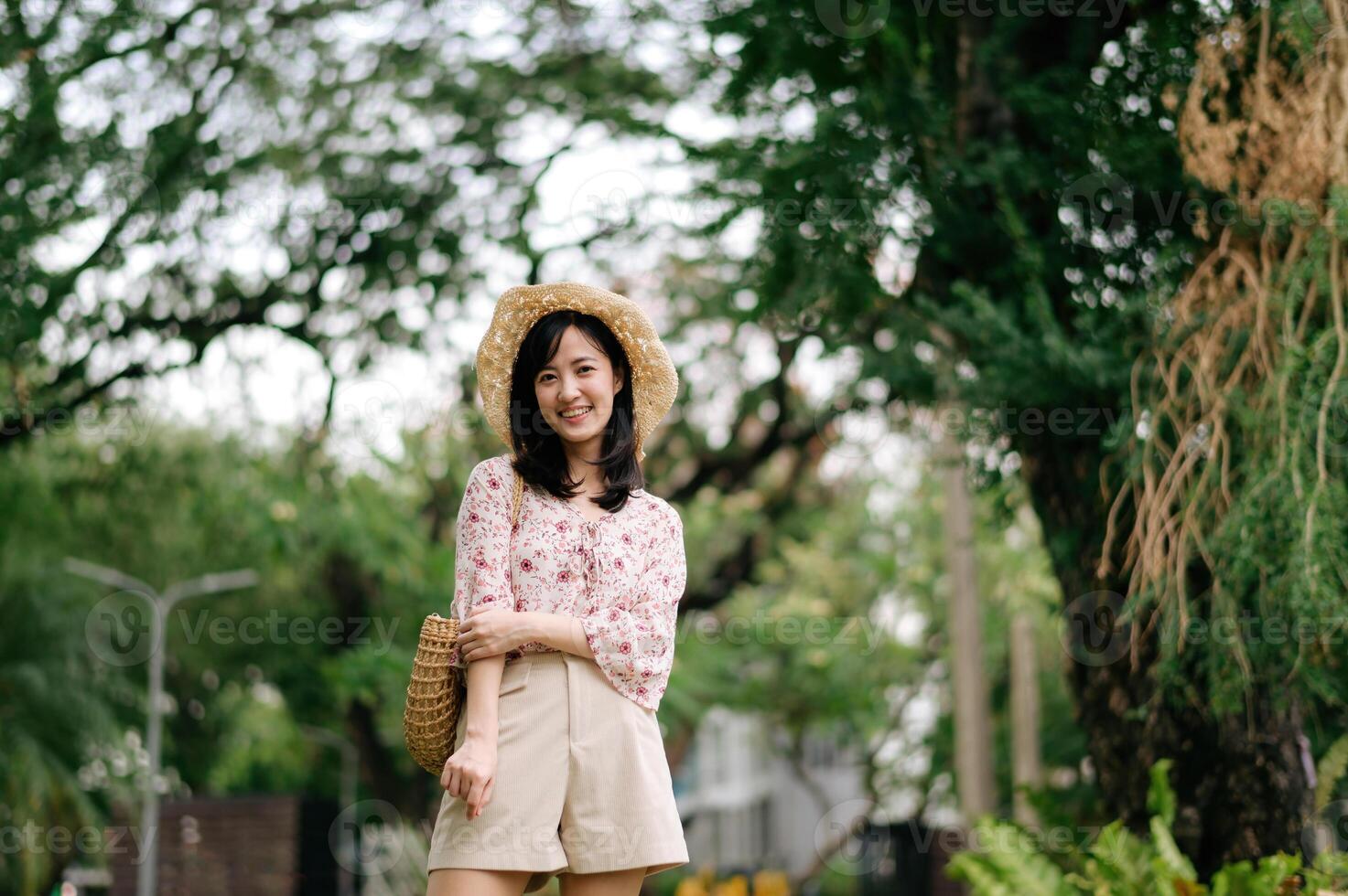 ritratto di asiatico giovane donna viaggiatore con tessitura cappello e cestino contento Sorridi su verde pubblico parco natura sfondo. viaggio viaggio stile di vita, mondo viaggio esploratore o Asia estate turismo concetto. foto