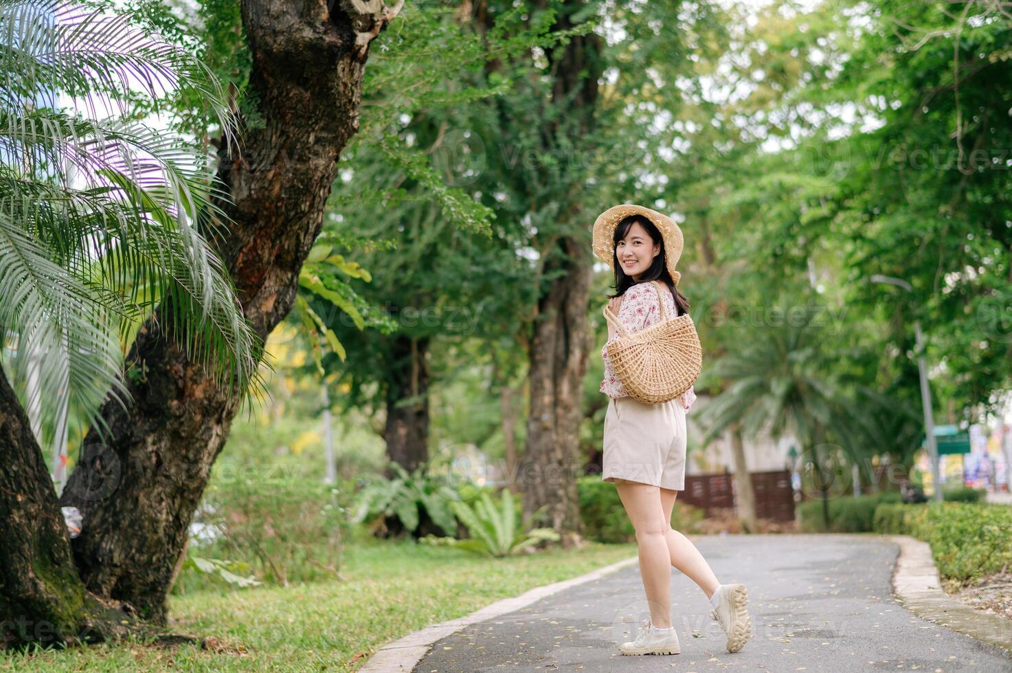 ritratto di asiatico giovane donna viaggiatore con tessitura cappello e cestino contento Sorridi su verde pubblico parco natura sfondo. viaggio viaggio stile di vita, mondo viaggio esploratore o Asia estate turismo concetto. foto