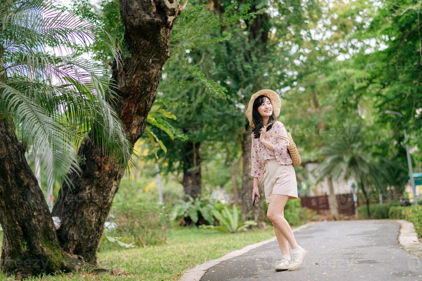 ritratto di asiatico giovane donna viaggiatore con tessitura cappello e cestino contento Sorridi su verde pubblico parco natura sfondo. viaggio viaggio stile di vita, mondo viaggio esploratore o Asia estate turismo concetto. foto