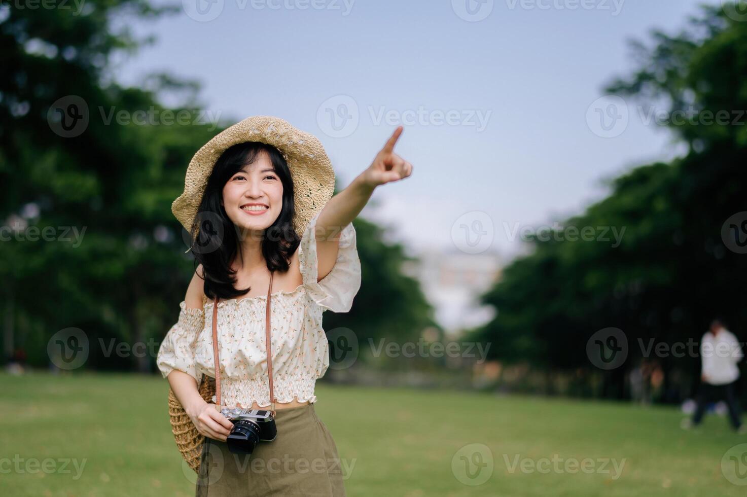 ritratto di asiatico giovane donna viaggiatore con tessitura cappello e cestino e un' telecamera su verde pubblico parco natura sfondo. viaggio viaggio stile di vita, mondo viaggio esploratore o Asia estate turismo concetto. foto