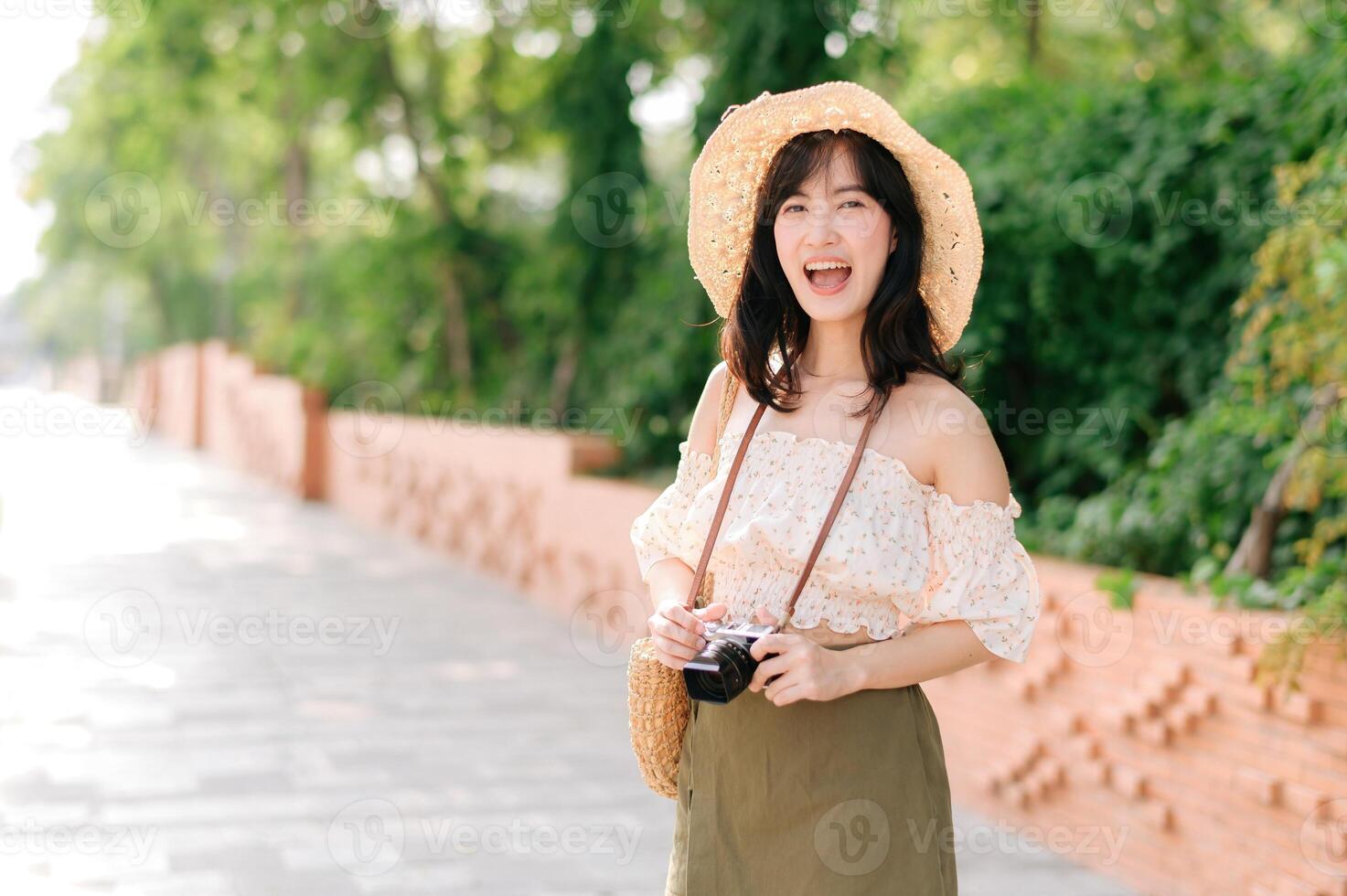 ritratto di asiatico giovane donna viaggiatore con tessitura cappello e cestino e un' telecamera su verde pubblico parco natura sfondo. viaggio viaggio stile di vita, mondo viaggio esploratore o Asia estate turismo concetto. foto