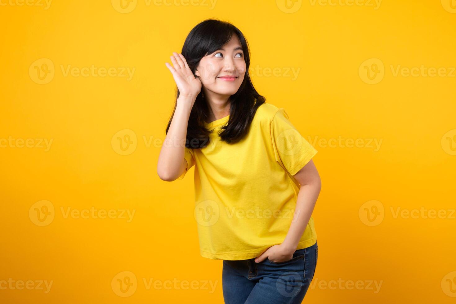 catturare Attenzione ritratto di giovane asiatico donna. indossare un' giallo maglietta e denim jeans, Leans nel per origliare e ascoltare, evocando curiosità e intrigo. cattura l'attenzione promozioni e sconti. foto