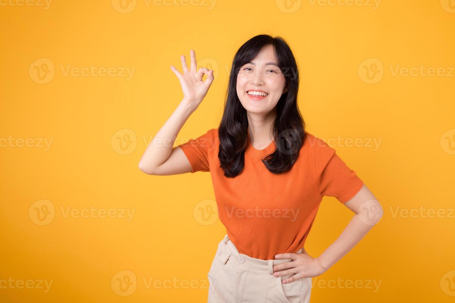 positivo asiatico donna nel sua 30s don arancia camicia, mostrando va bene cartello su giallo sfondo. mani gesto concetto. foto